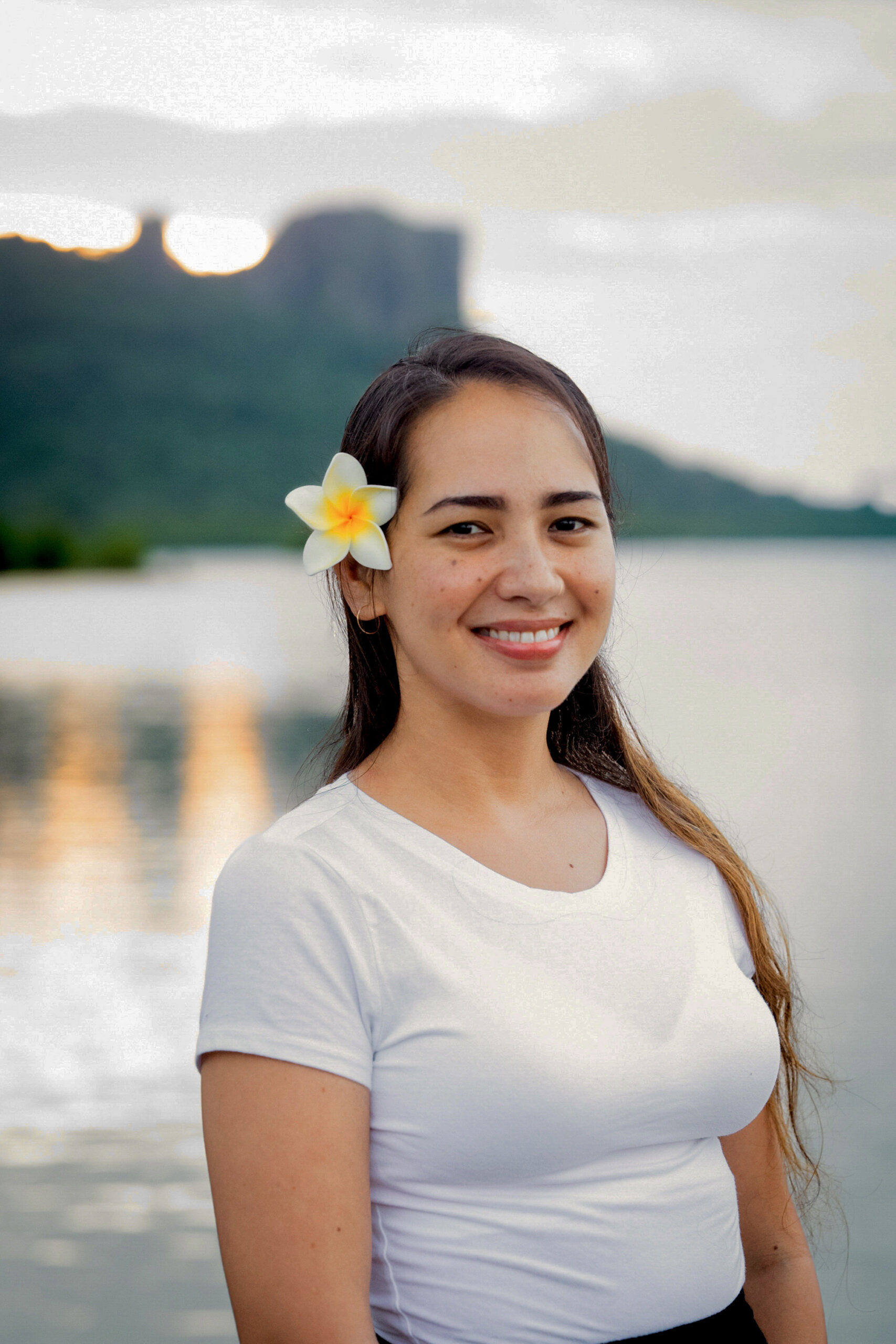 Jasmine Mendiola, a smiling Pohnpeian woman with a flower in her hair, in front of the bay in Kolonia, Pohnpei. 